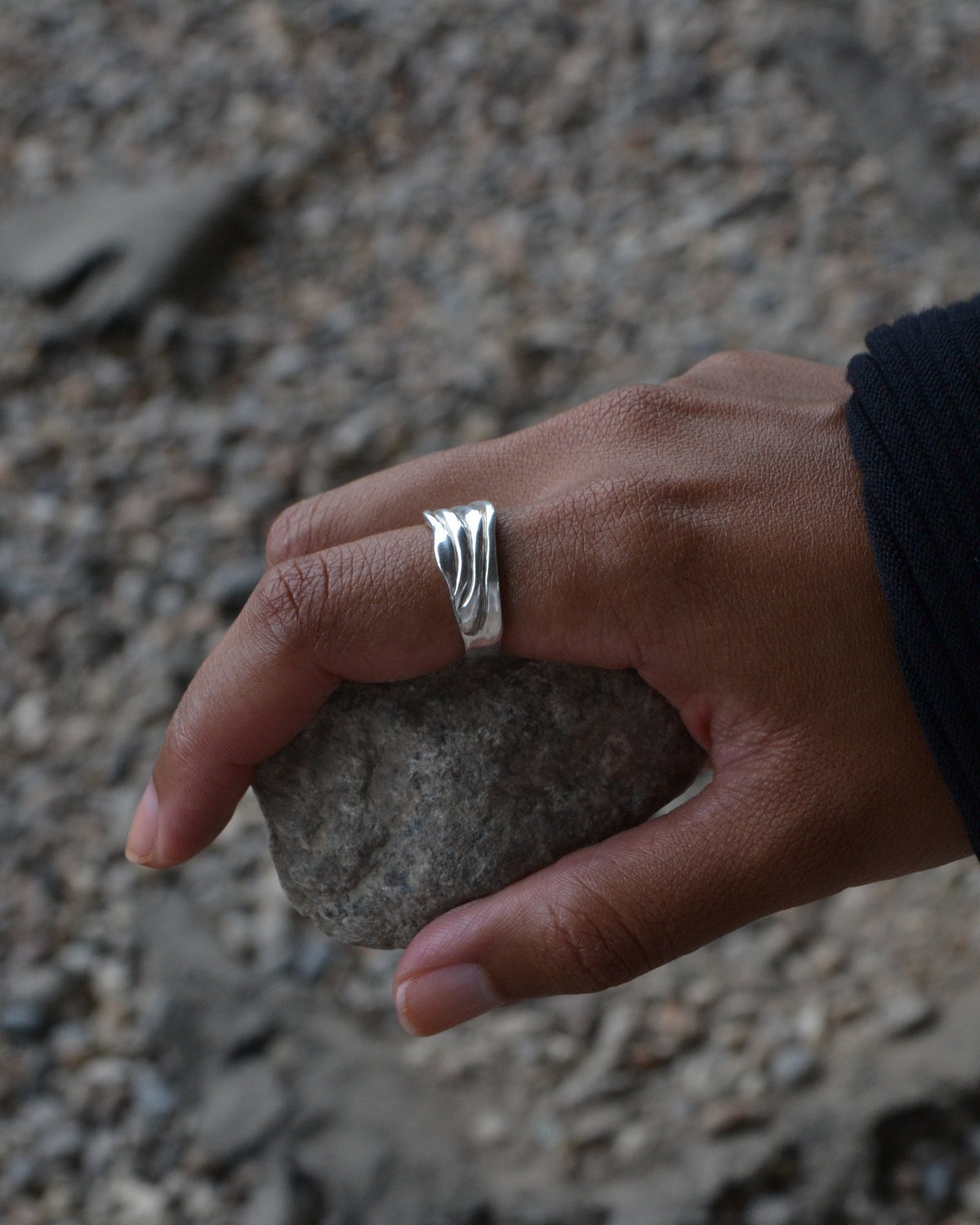 Blurr Ring worn on a hand holding a stone on gravel